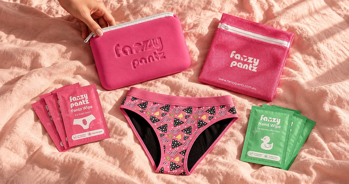Fanzy Pantz starter kit contents laid out on pastel bedding: pouch, laundry bag, undies and wipes