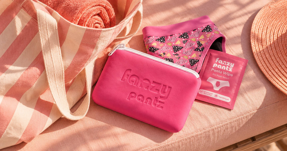 Fanzy Pantz pouch, undies and wipes in a striped beach bag next to a straw hat